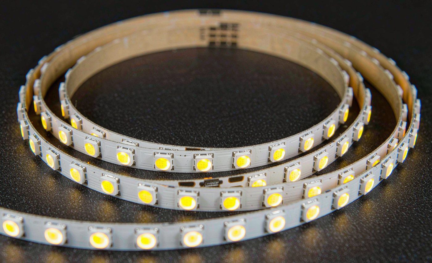 Macro photograph of a coiled SMD LED strip: individual rectangular diodes with phosphor domes spaced evenly along a white PCB